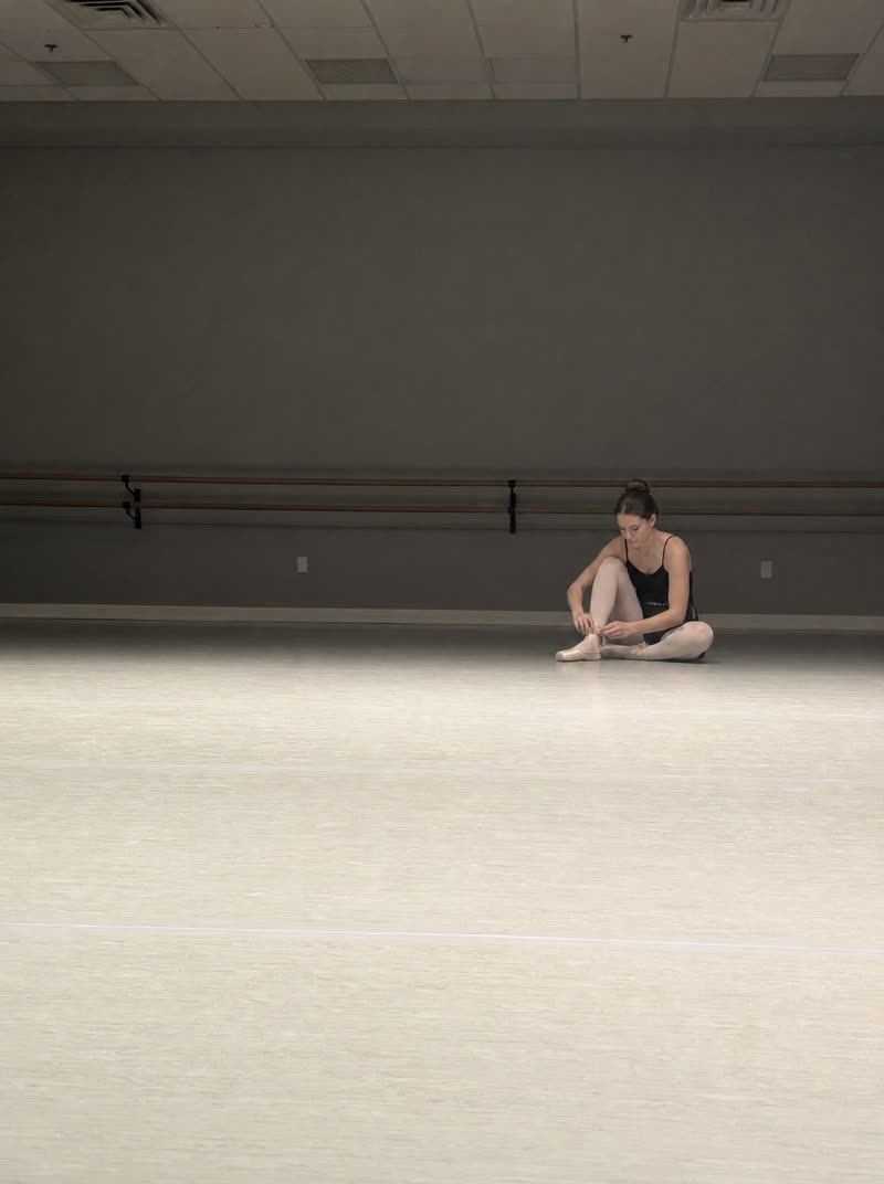 a dancer lacing shoes in an empty studio — as shot